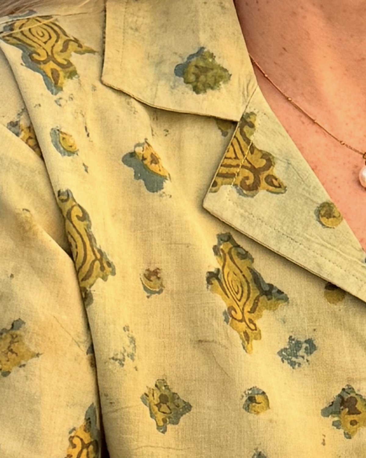 The collar of a pale yellow cotton shirt, block printed with mustard and green motifs