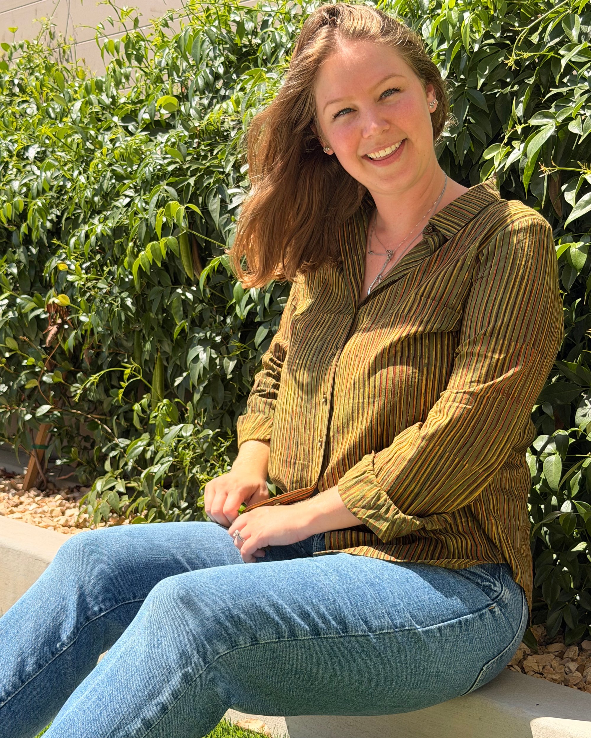 A woman in a striped cotton shirt sitting in a sunlit garden